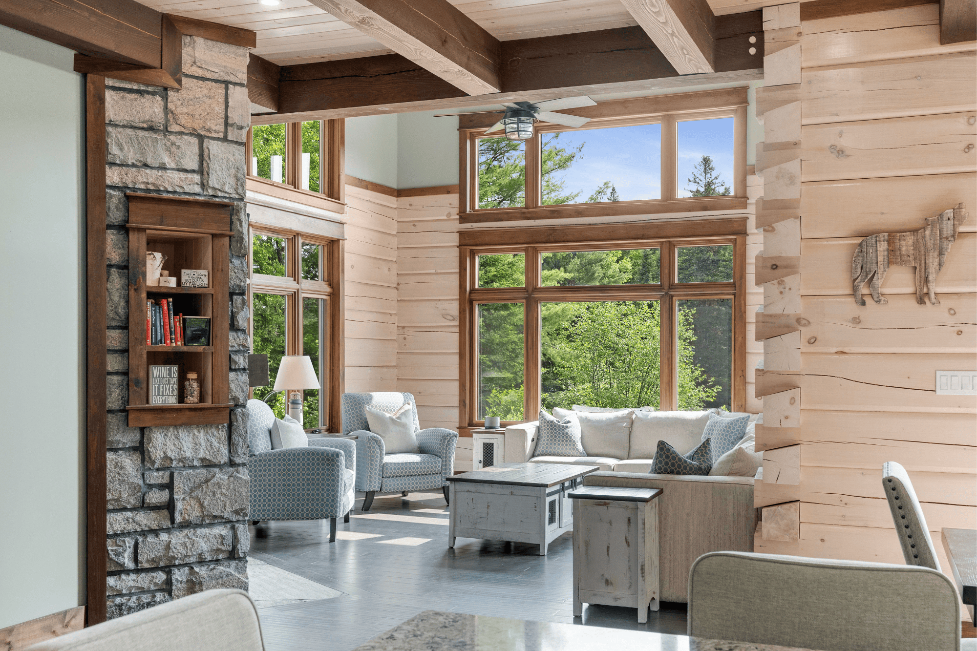 The great room of the award-winning Riverview by True North Log & Timber Homes. A home designed with whitewashed log walls, 2 extra courses of log, and large windows to create a bright and airy living space.